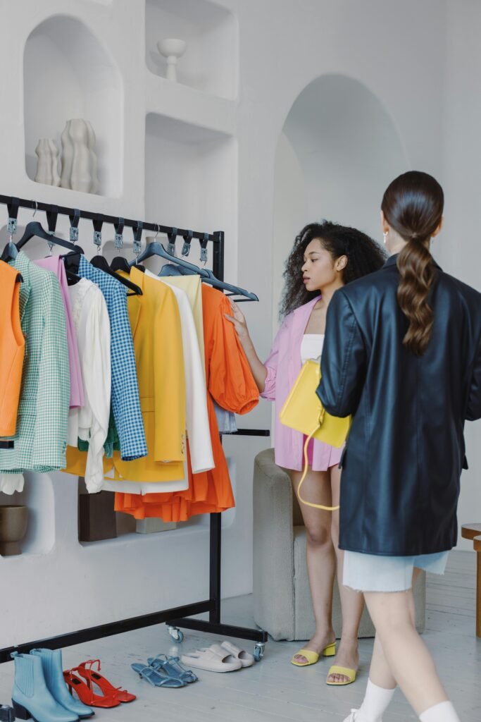 Fashion stylists coordinating outfits in a chic boutique with vibrant apparel selection.